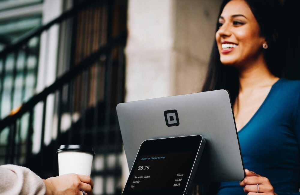 A coffee shop owner smiles as her customer pays at the register.